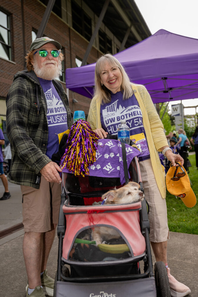 Two people with a stroller with two dogs in it.