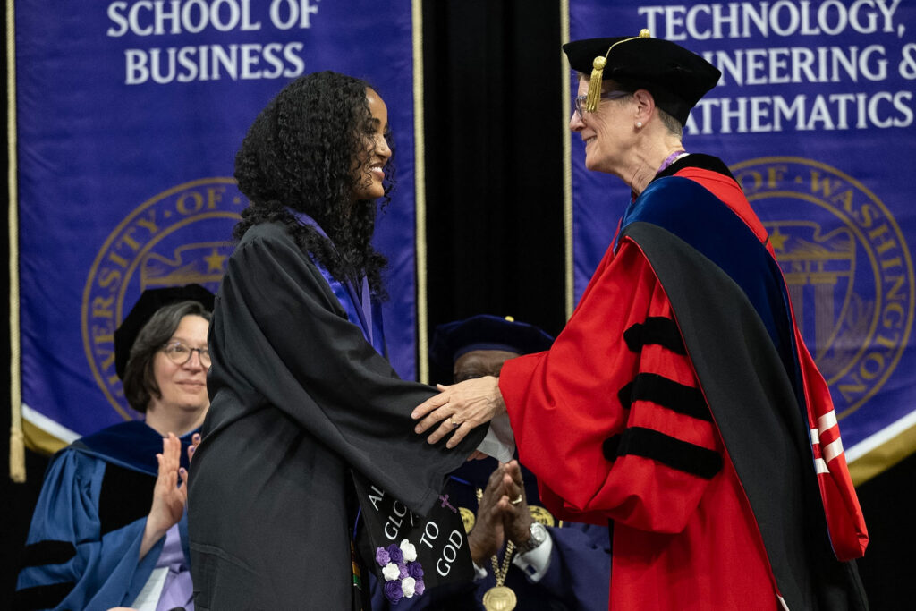 Two people in commencement regalia shaking hands.