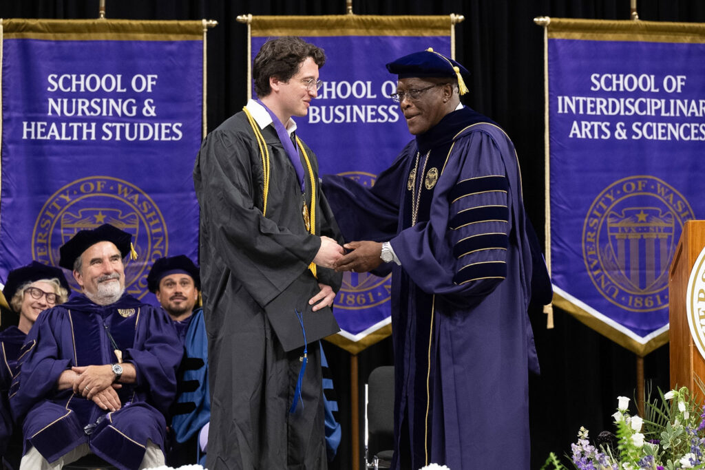 Two people in commencement regalia shaking hands.