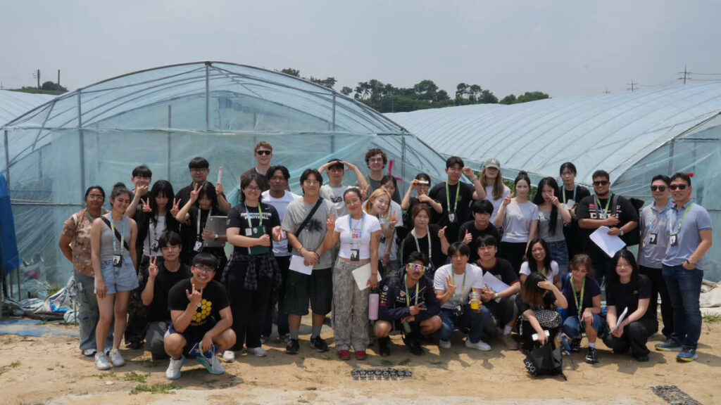 A group of people pose together in front of a greenhouse.