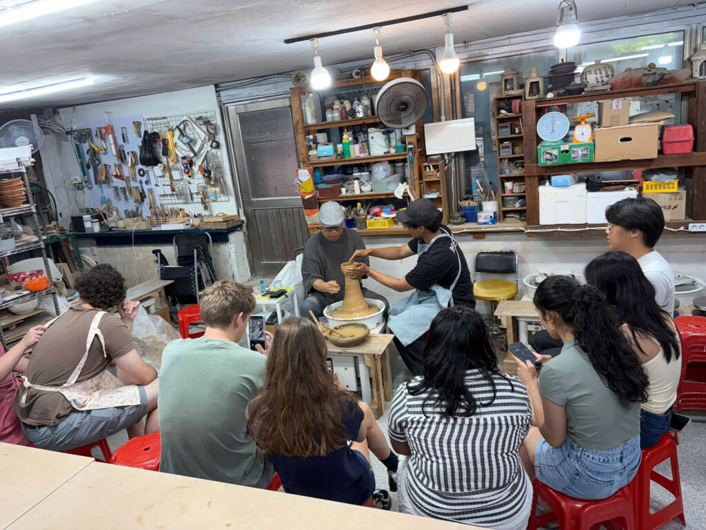 A group of people watch a potter at a potting wheel. 
