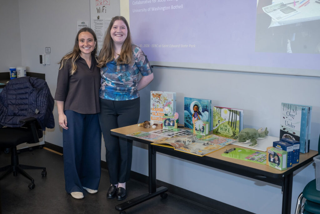Two people stand next to a table with books on it.