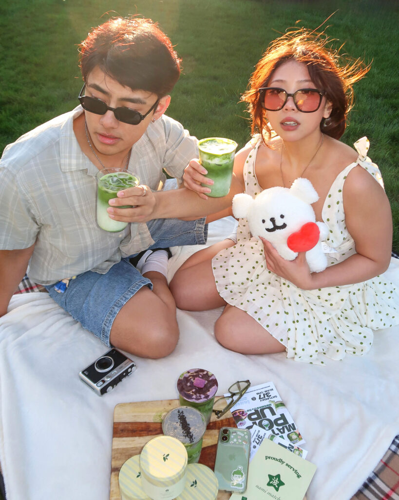 Two people holding matchas on a picnic blanket.