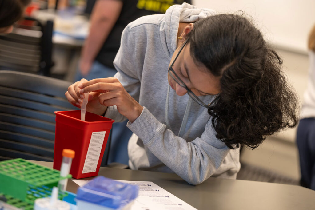A person drawing a substance from a container using a pipette.