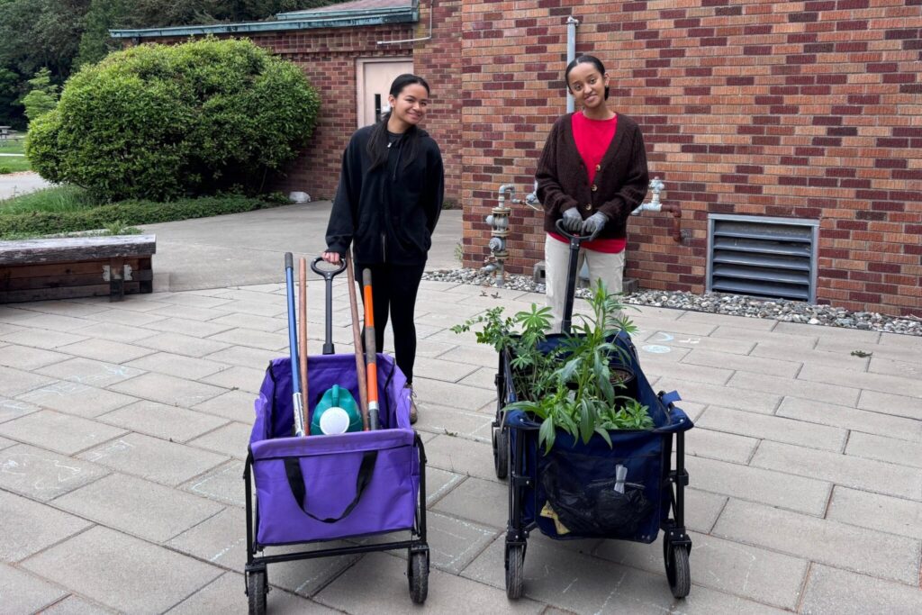 Two people pull wagons with plants and gardening supplies in them.