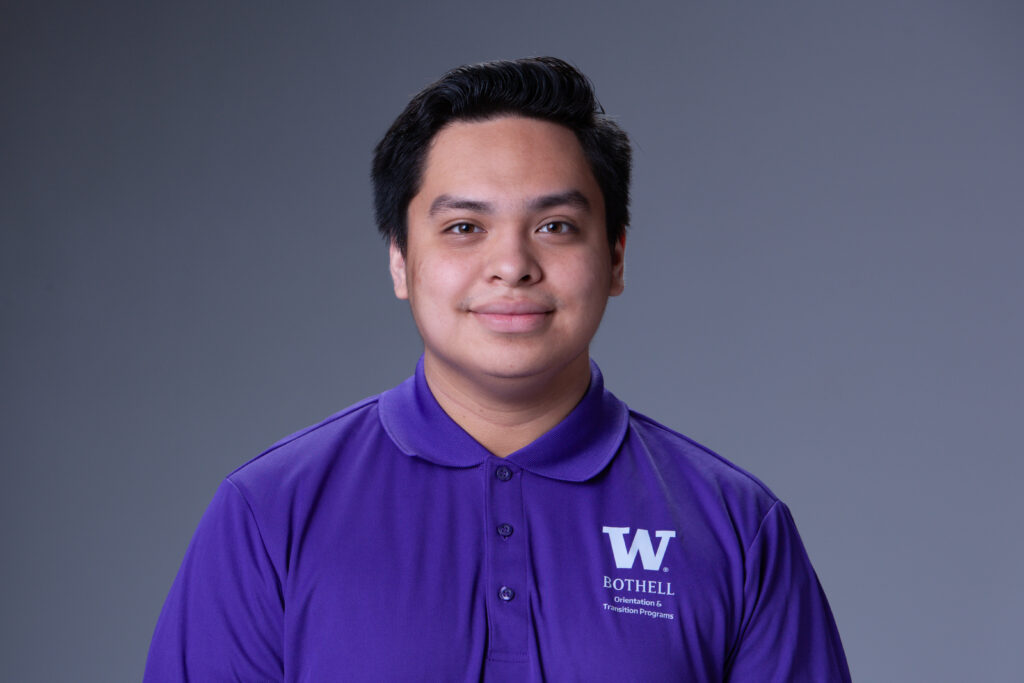 Orientation Leader Jorge wearing a purple polo in front of a gray background