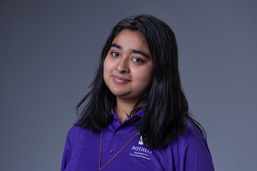 Orientation Leader Meem wearing a purple polo in front of a gray background