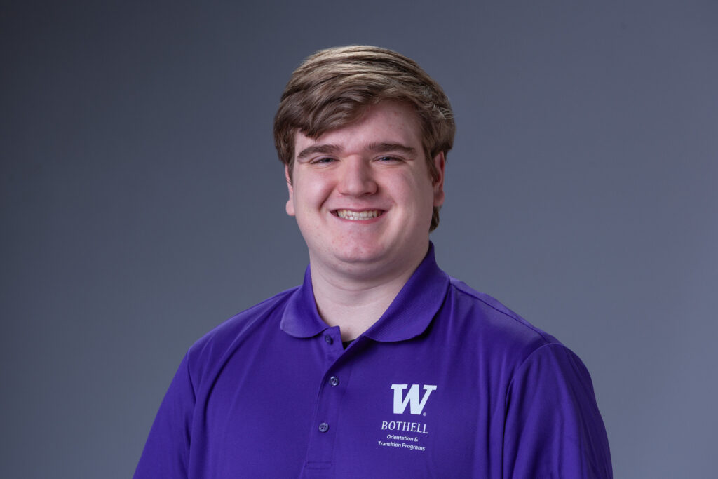 Orientation Leader Peter wearing a purple polo in front of a gray background