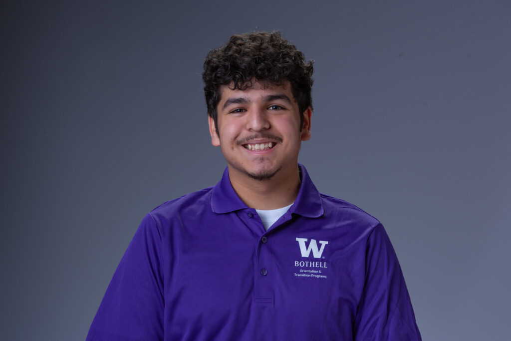 Orientation Leader Santiago wearing a purple polo in front of a gray background