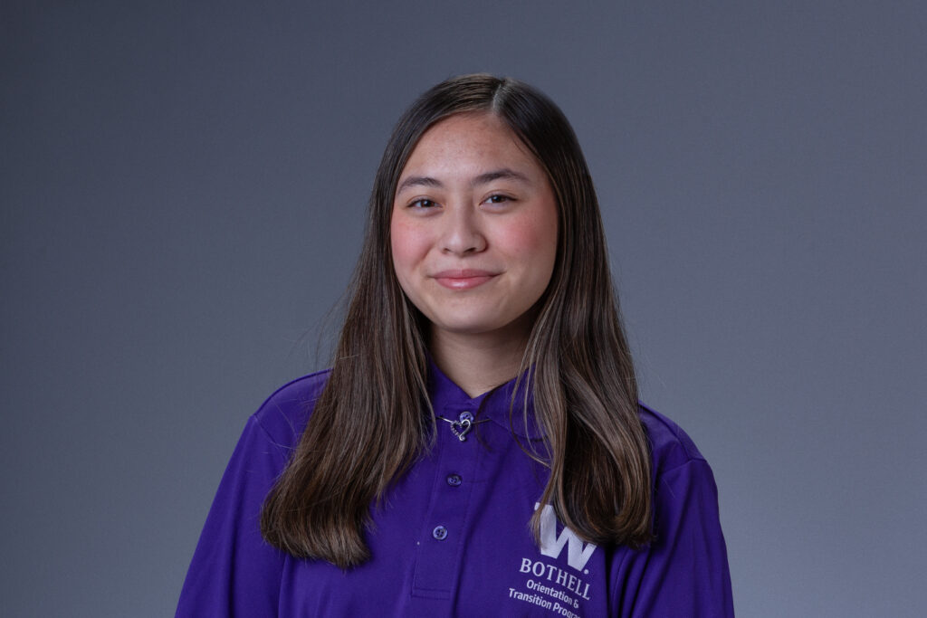 Peer Coach Daniela in a purple polo in front of a gray background
