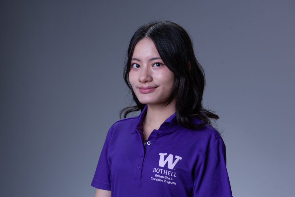 Peer Coach Grace in a purple polo in front of a gray background