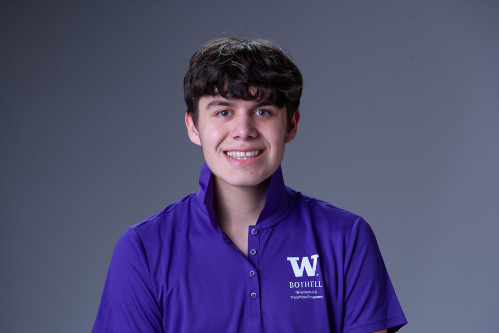Peer Coach Aiden in a purple polo in front of a gray background