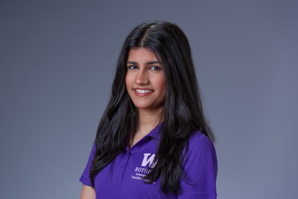 Peer Coach Jiya in a purple polo in front of a gray background