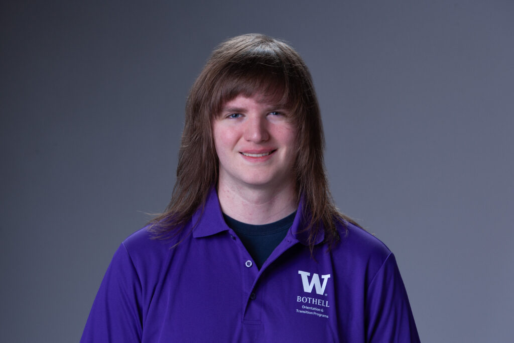 Peer Coach John in a purple polo in front of a gray background