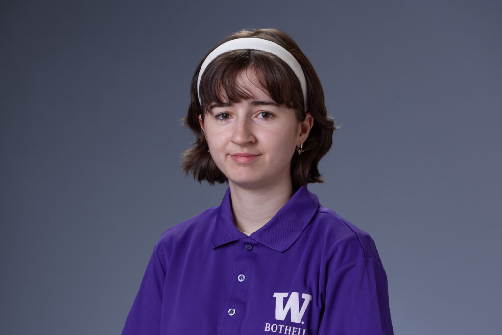 Peer Coach Mary in a purple polo in front of a gray background