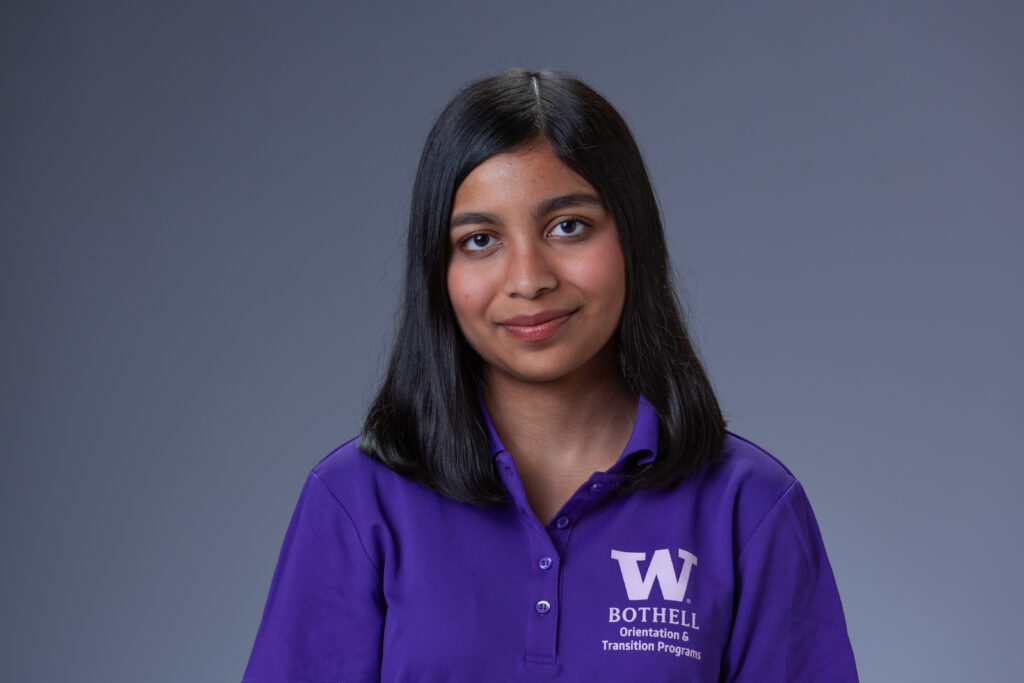 Peer Coach Mishti in a purple polo in front of a gray background