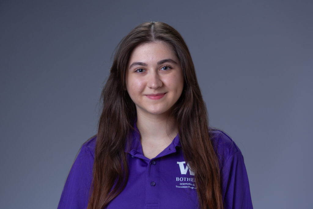 Peer Coach Alexandra in a purple polo in front of a gray background