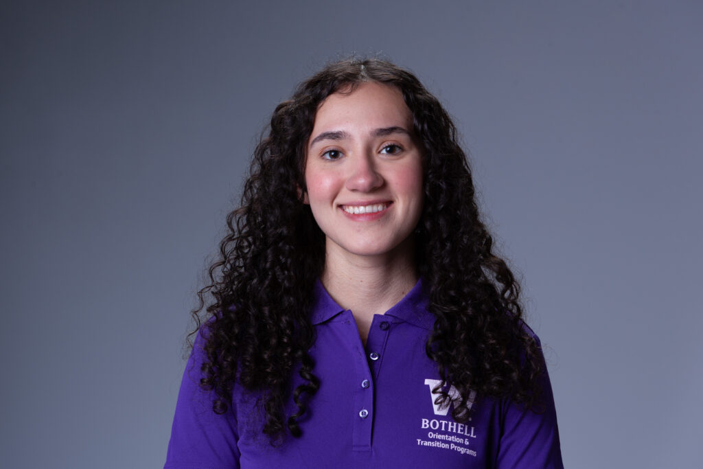 Peer Coach Angie in a purple polo in front of a gray background