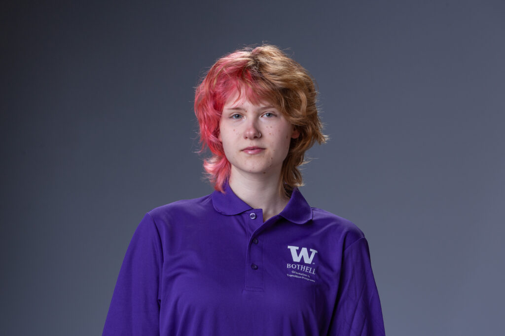 Peer Coach Aster in a purple polo in front of a gray background