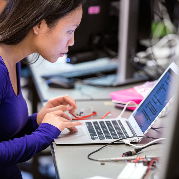 Woman with dark hair wearing a long sleeved purple shirt working on a computer.