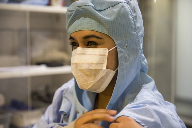 Malia Steward wearing a blue bunnysuit and white mask prepping to go into a cleanroom.