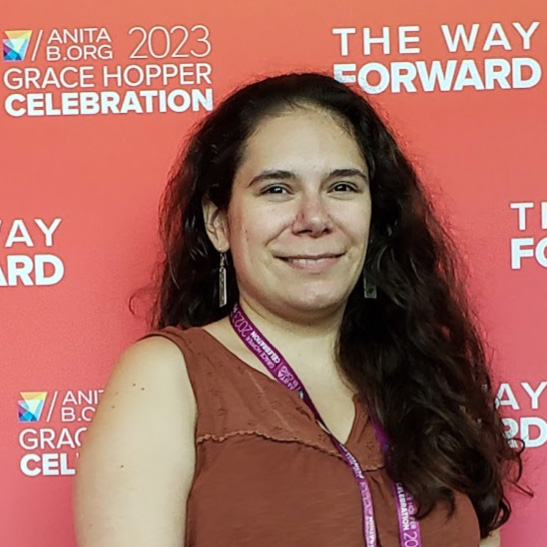 Breanna Powell posing for a photo in front of the Anita.org 2023 Grace Hopper Celebration, THE WAY FORWARD orange backdrop.