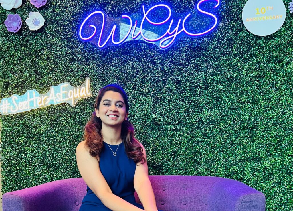 Rithi Afra Jerald Jothi at the Women in Cybersecurity conference next to LED signs that say "#SeeHerAsEqual" and "WiCyS."