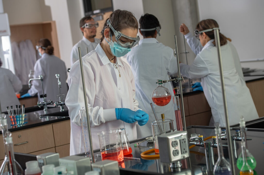 Students in the lab working with beakers of orange, red and green solutions.