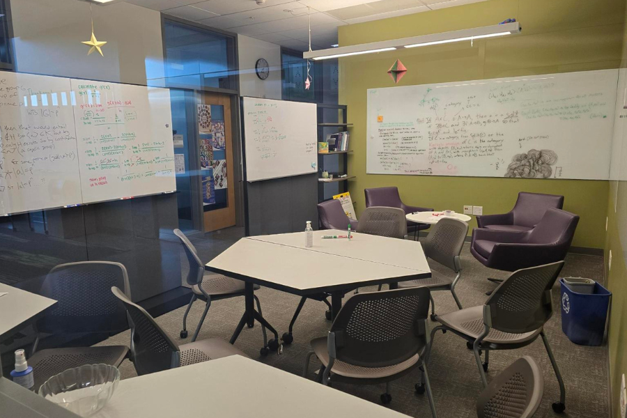 The Math Lounge, featuring hexagon tables with rolling chairs, four purple soft chairs around a round table, and whiteboards lining the walls.