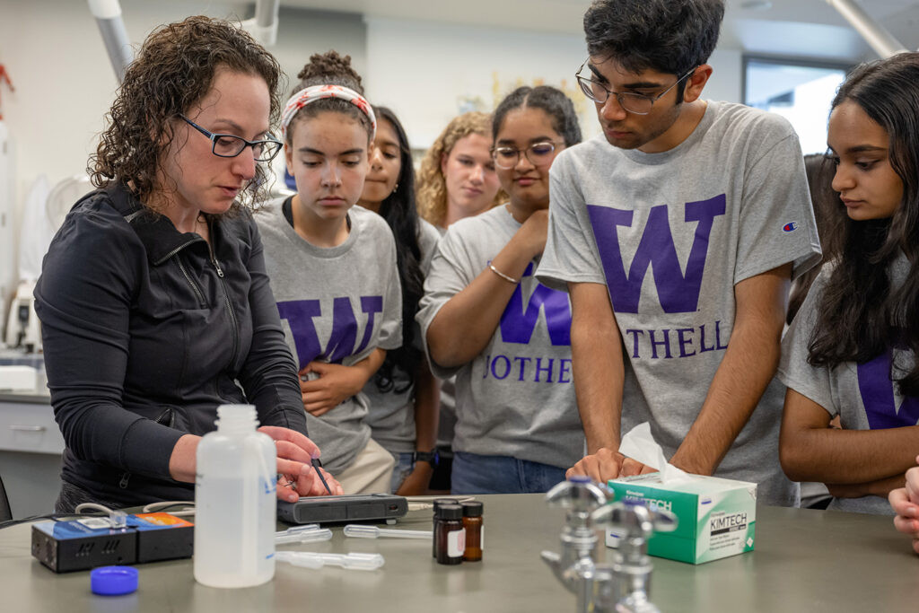 Students gather around Dr. Lori Robins as she does a chemistry demonstration.