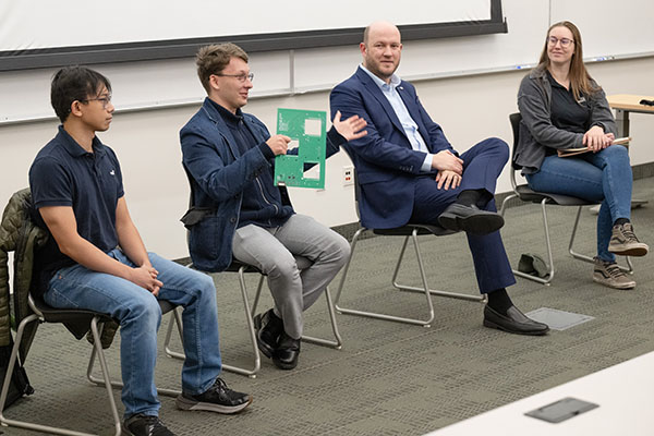Panel of four alumni sitting at the front of class in chairs.