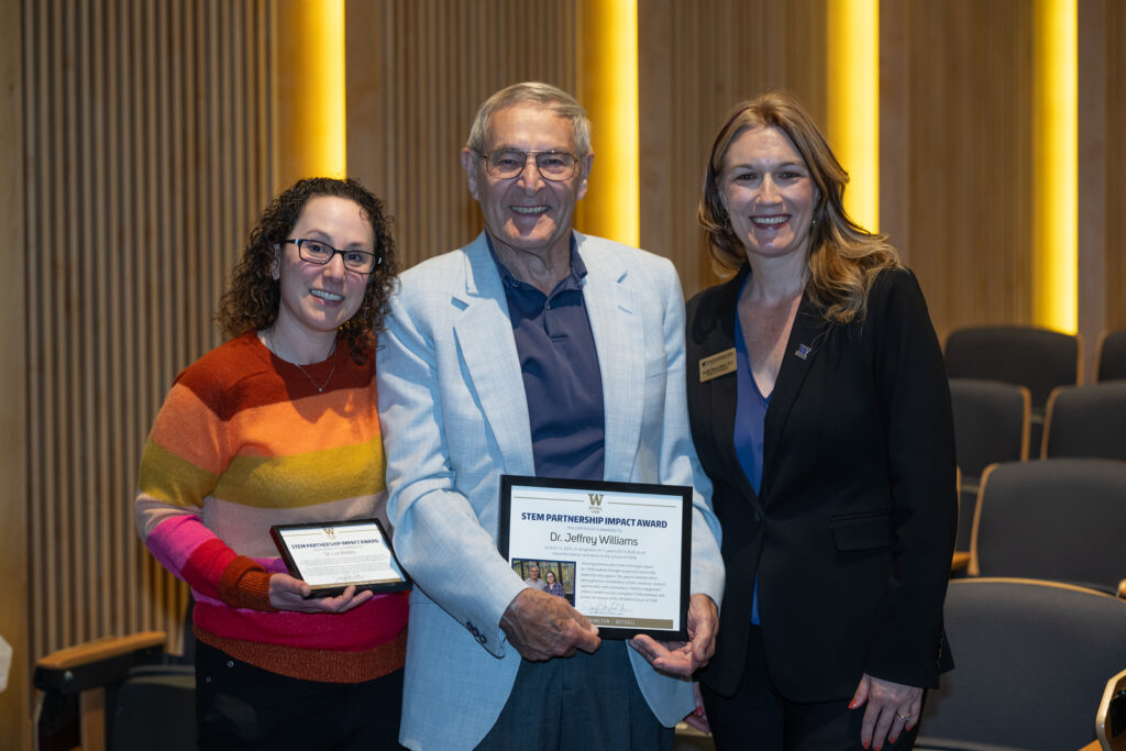 Dr. Lori Robins holds a small framed certificate alongside Dr. Jeffrey Williams who holds a larger certificate alongside Dean Jennifer McLoud-Mann at the awards ceremony.