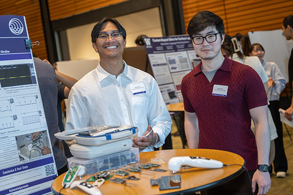 Two students in front of capstone poster with their prototype on display.