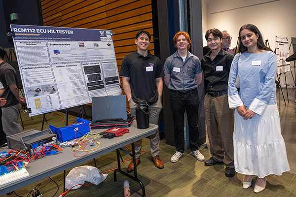 Group of four students next to their poster presentation and prototype display.
