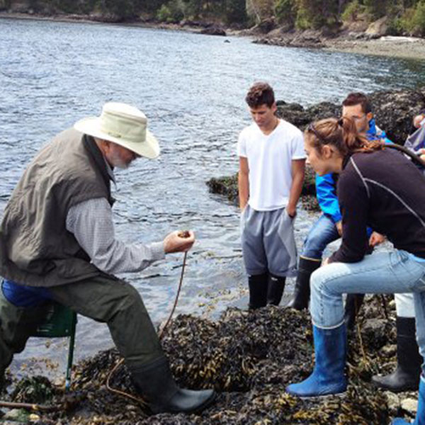 Students and researchers with boots on looking at a specimen near the water