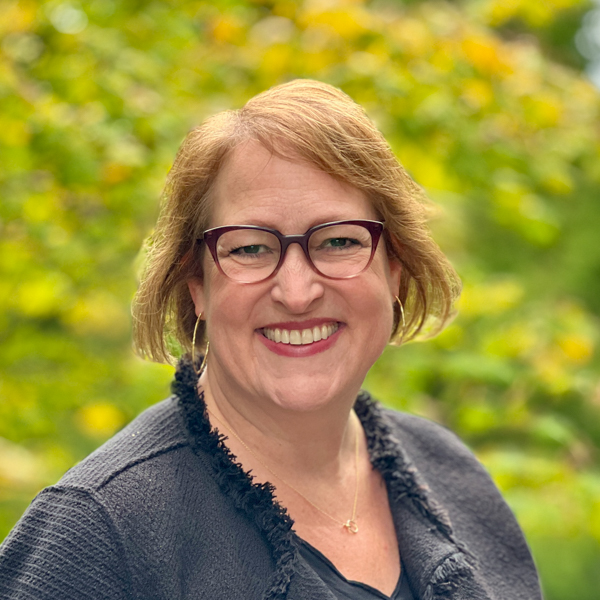 White woman with short blond hair who is wearing a black sweater and glasses.