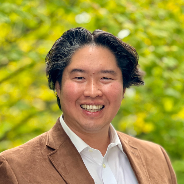 Asian man with dark hair wearing a brown blazer over a white button down shirt.