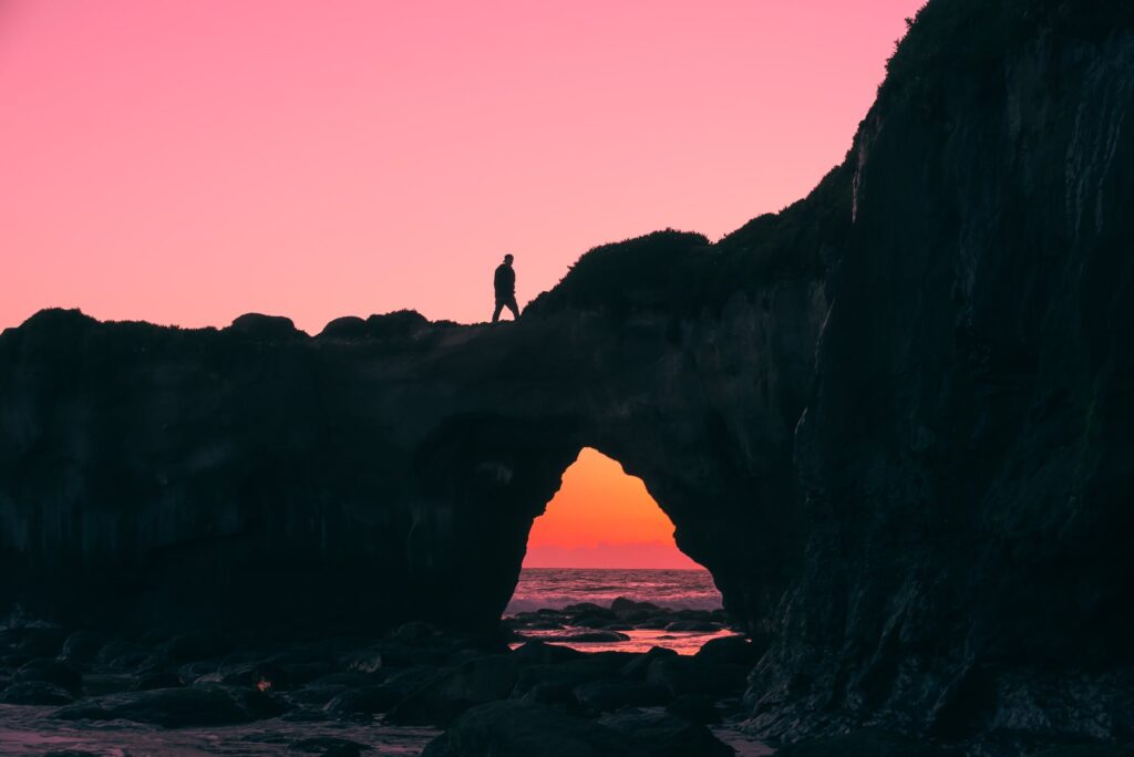 Person walking over a natural bridge with sunset in the background
