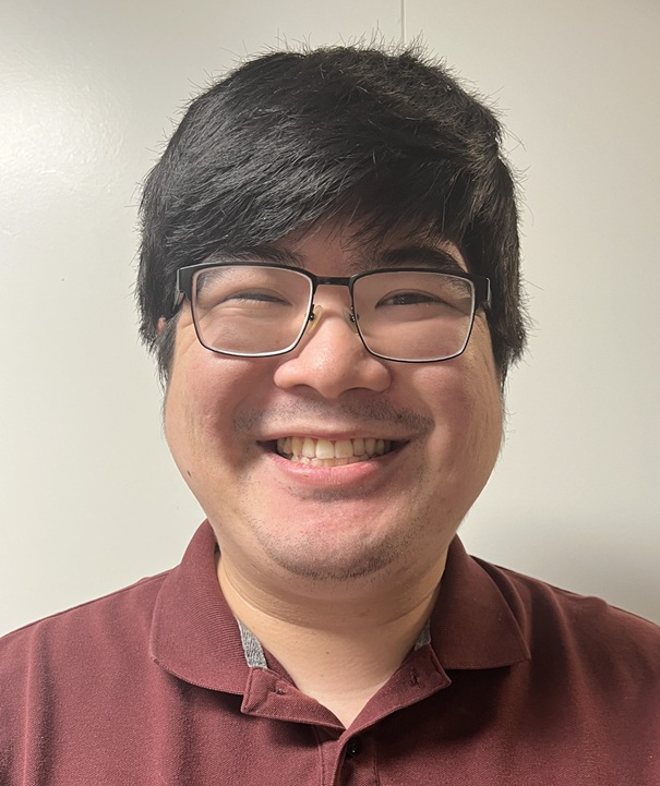 Japanese man with short black hair and brown eyes who is wearing a red and blue collared shirt. 