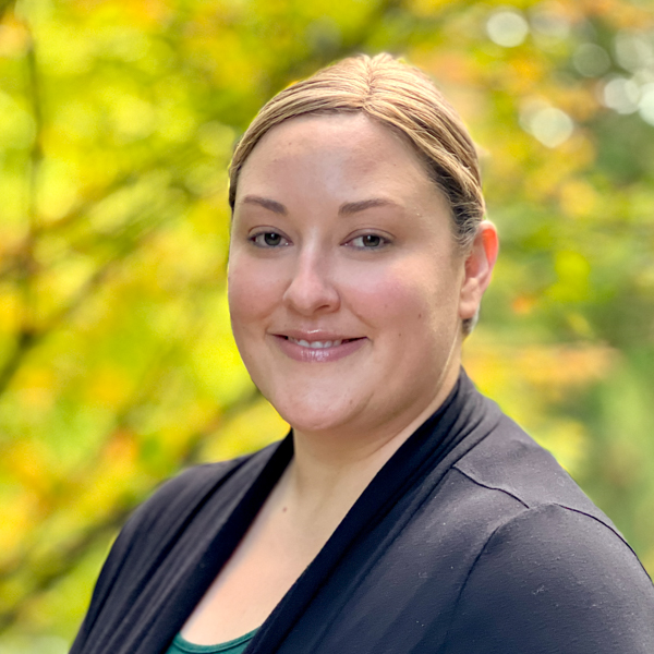 Woman with brown eyes and short blond hair wearing a black sweater over a teal shirt.