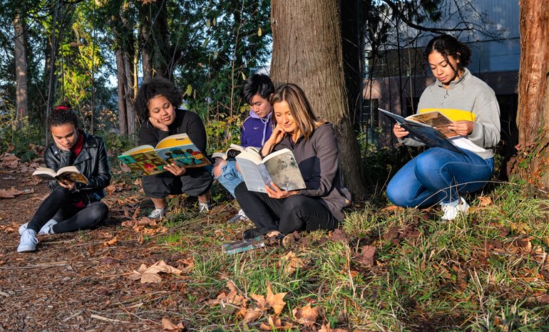Students with books in forest.