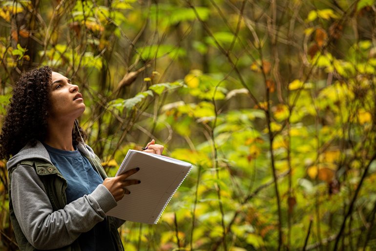 Student with pen and paper in forest.