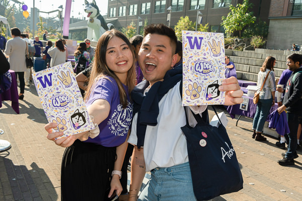 Two students smiling and holding up their W Day stickers on the plaza.