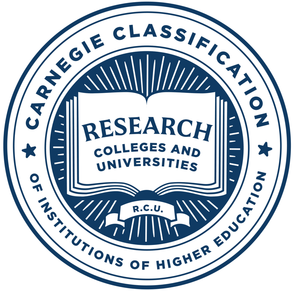 Logo for the Carnegie Classification of Institutions of Higher Education. The outside of the seal has the name of the organization. The inside of the seal reads "Research Colleges and Universities" on an open book graphic and "R.C.U." on a banner beneath the book.