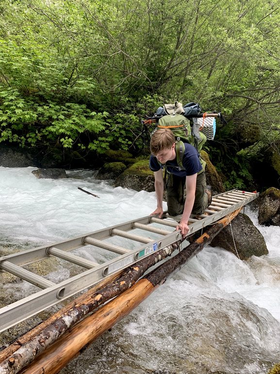 Alex Wachter crossing stream on ladder.