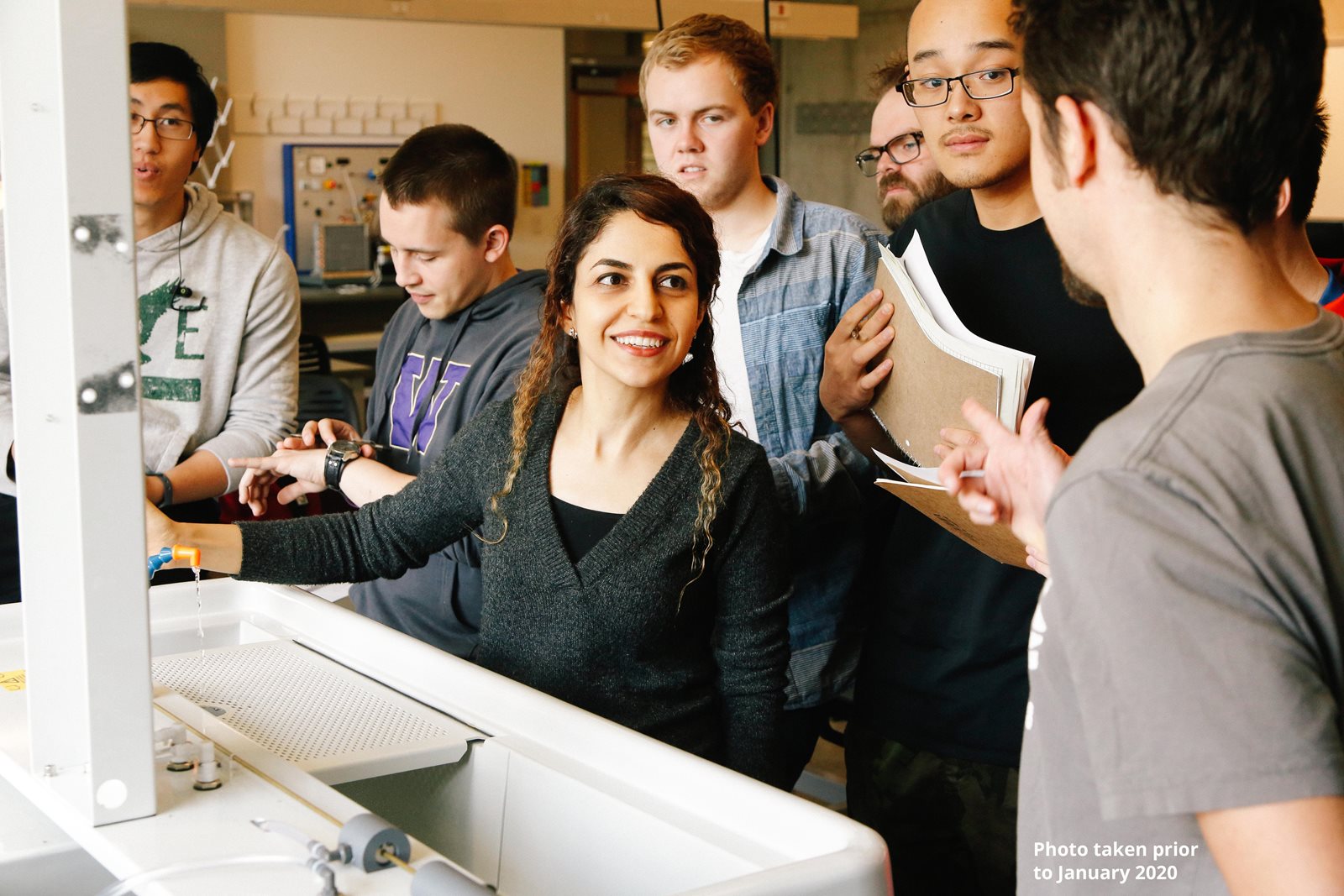 Shima Abadi with a group of students in a classroom huddled around a whiteboard