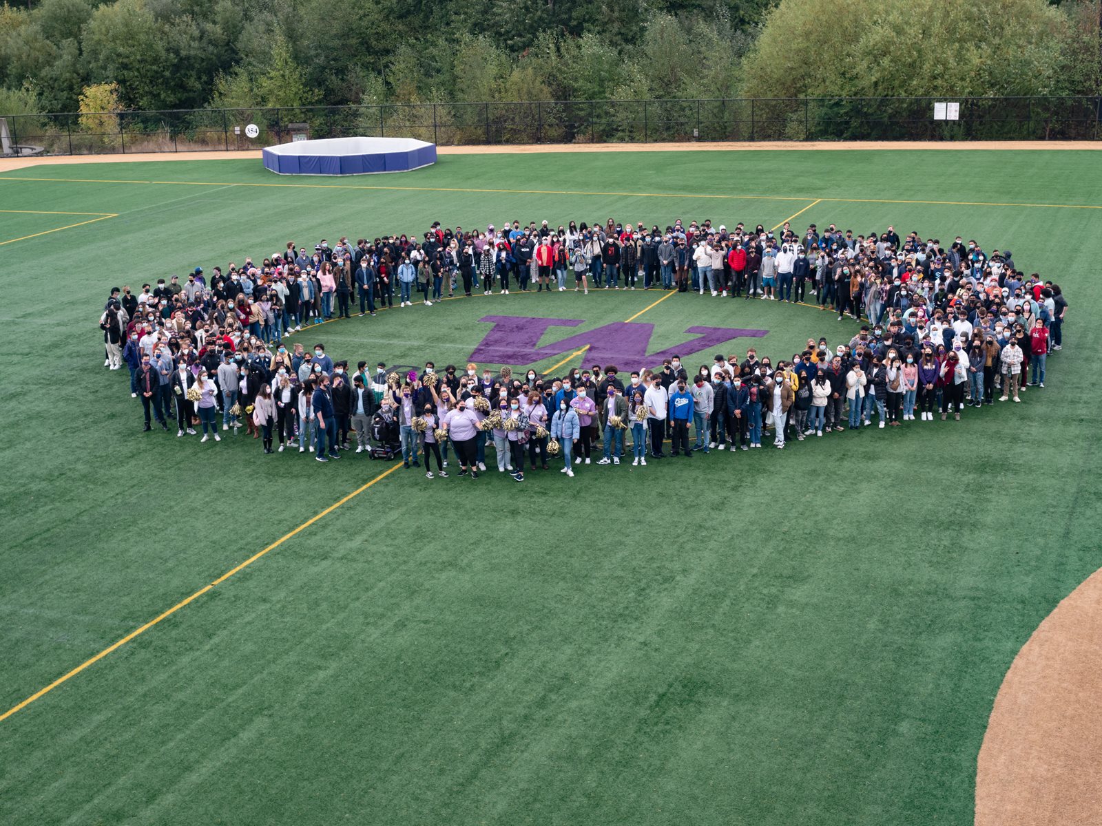 Students standing in a circle on the field around the W