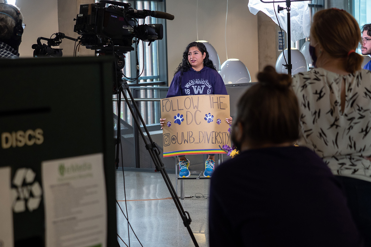 Diana holding a sign reading follow the Diversity Center at UWB_Diversity while being filmed