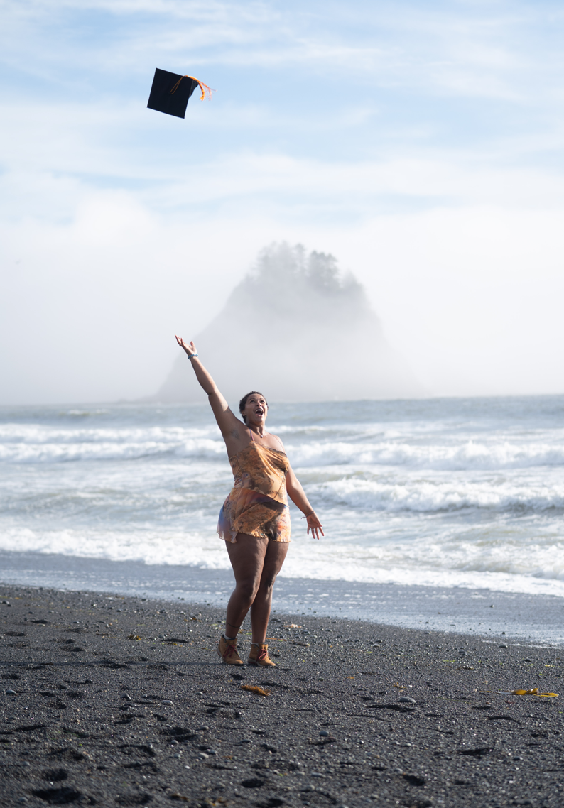 Tay Verville tossing her graduation cap into the air at a beach